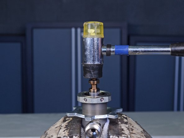 With the pump cylinder still in the vise, use a mallet to gently tap down on the top of the piston rod to loosen it from the pump cylinder.