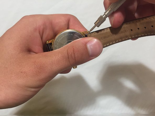 Press down and compress the spring. By pushing the bar away from the body, one end of the spring bar should come loose.