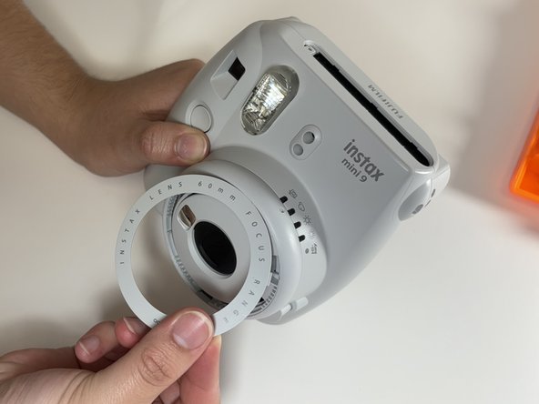 Fujifilm Instax Mini 9 Flash Capacitor Replacement, Pry Off the Lens Shroud: crwdns2935265:06crwdnd2935265:02crwdnd2935265:02crwdne2935265:0