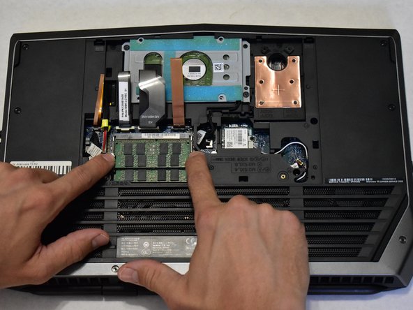 Find the RAM located near the edge of the computer closest to you. Locate the small latches on either side of the RAM stick and push in the two latches to release. Gently grasp the RAM stick on either side and pull straight out. Repeat for the second RAM stick.