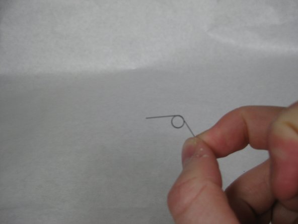 Carefully lift the &quot;Y&quot; shaped plastic piece from its pin and pull the spring from the pin as it is removed.